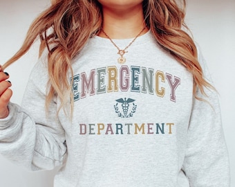 May include: A gray sweatshirt with the text "EMERGENCY DEPARTMENT" in colorful letters. The text is in an arch shape with a medical symbol in the center.