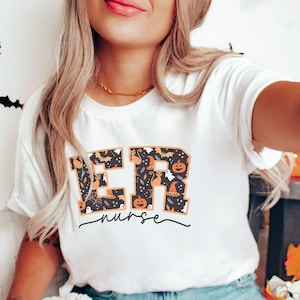 May include: White t-shirt with the letters "ER" in black with a Halloween-themed pattern of pumpkins, bats, ghosts, and witches' hats. The text "nurse" is written in cursive below the letters.