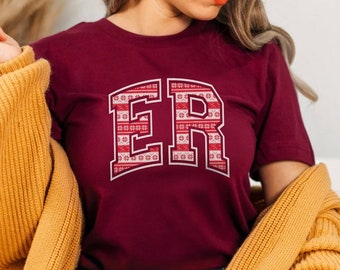 May include: A maroon t-shirt with a white outline of the letters "ER" in a red and white holiday pattern.