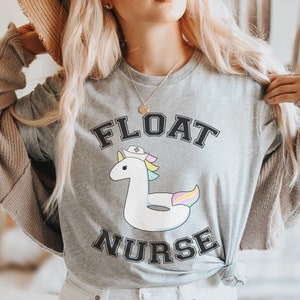 Peut inclure: T-shirt gris avec un motif de licorne flottante avec un bonnet d'infirmière et le texte "FLOAT NURSE".