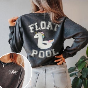 May include: A dark gray sweatshirt with the text "FLOAT POOL" in white letters with a white unicorn pool float with rainbow accents. The sweatshirt has a small white text on the front that says "FLOAT pool" in cursive.