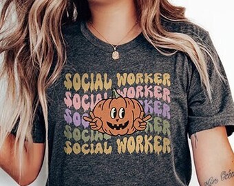 May include: A dark gray t-shirt with a graphic of a smiling pumpkin and the text "SOCIAL WORKER" repeated in different colors.