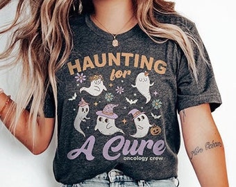 May include: A gray t-shirt with a graphic of ghosts and the text "Haunting for a Cure" with the words "oncology crew" below. The shirt is being worn by a person with long blonde hair.