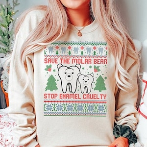 May include: A cream-colored sweatshirt with a Christmas-themed design featuring two white polar bear teeth with the text "Save the Molar Bear" and "Stop Enamel Cruelty".