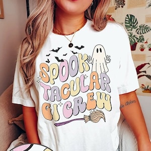 May include: White t-shirt with a colorful graphic that says "Spooktacular Crew" with a ghost and bats. The graphic has a distressed effect.