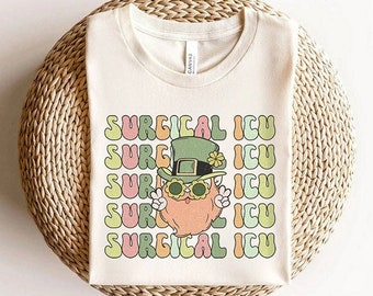 May include: A white t-shirt with a green, orange, and yellow graphic of a cartoon leprechaun wearing a green hat and sunglasses. The text "SURGICAL ICU" is repeated in a rainbow pattern on the shirt.