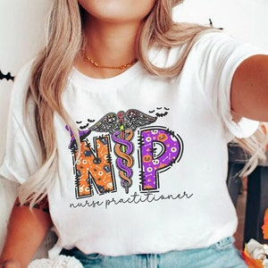 May include: White t-shirt with a Halloween-themed design featuring the letters "NP" with a caduceus symbol in the middle. The letters are decorated with Halloween-themed patterns like pumpkins, bats, and ghosts. The text "nurse practitioner" is written below the design.