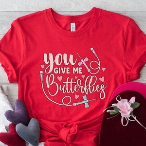 May include: Red t-shirt with the text "You give me butterflies" in pink and white lettering. The text is surrounded by a graphic of a medical IV drip and hearts.