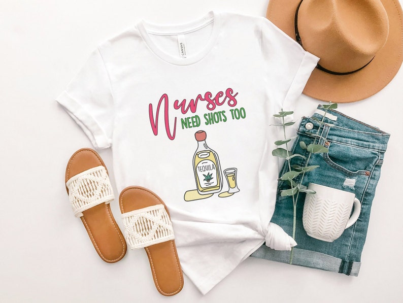 May include: White t-shirt with the text "Nurses need shots too" in pink and green lettering. A cartoon image of a bottle of tequila and a shot glass are below the text.