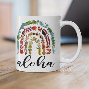 May include: White ceramic coffee mug with a colorful illustration of Hawaiian-themed items arranged in a rainbow shape. The text "aloha" is printed in black below the illustration.