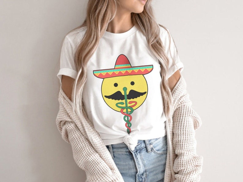 K&ouml;nnte beinhalten: Ein wei&szlig;es T-Shirt mit einem gelben Smiley, der einen roten, gr&uuml;nen und gelben Sombrero tr&auml;gt. Der Smiley hat einen schwarzen Schnurrbart und eine gr&uuml;ne Schlange kommt aus seiner Nase.