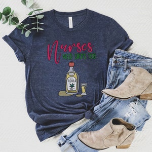 May include: A navy blue t-shirt with the text "Nurses need shots too" in red and green. A cartoon image of a bottle of tequila and a shot glass is below the text.