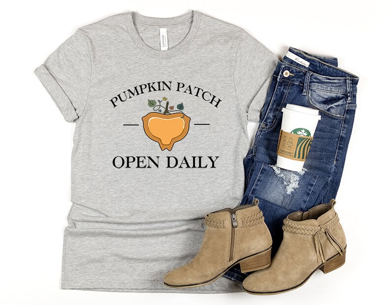 K&ouml;nnte beinhalten: Ein graues T-Shirt mit dem Text "Pumpkin Patch Open Daily" und einer stilisierten K&uuml;rbisgrafik.