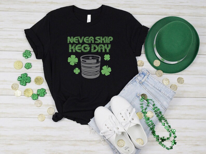 May include: Black t-shirt with the text "Never Skip Keg Day" in white letters. A silver keg is pictured below the text with green shamrocks on either side.