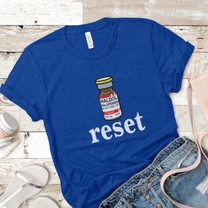 Peut inclure: T-shirt bleu roi avec un dessin d'un flacon de m&eacute;dicament portant l'inscription "HALDOL HALOPERIDOL INJECTION USP" et le mot "reset" en blanc. Le t-shirt est en tissu doux, id&eacute;al pour un usage quotidien.