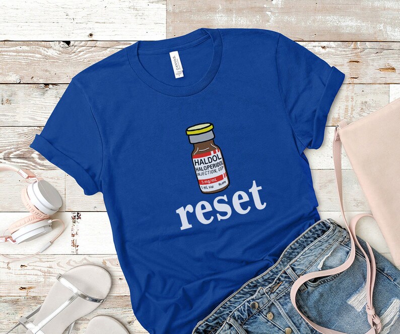 Peut inclure: T-shirt bleu roi avec un dessin d'un flacon de m&eacute;dicament portant l'inscription "HALDOL HALOPERIDOL INJECTION USP" et le mot "reset" en blanc. Le t-shirt est en tissu doux, id&eacute;al pour un usage quotidien.