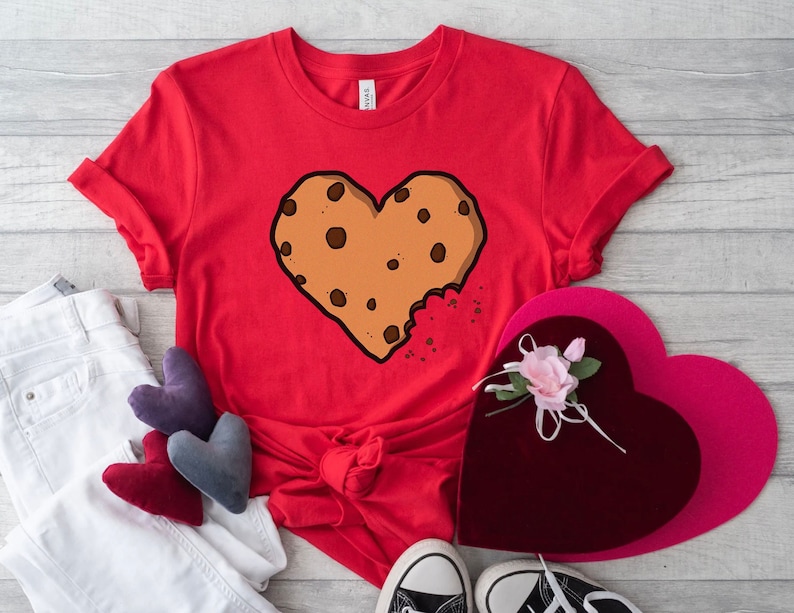 May include: Red t-shirt with a brown chocolate chip cookie shaped like a heart with a bite taken out of it.