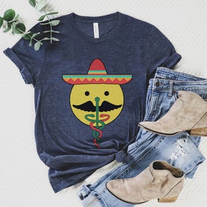 K&ouml;nnte beinhalten: Ein marineblaues T-Shirt mit einem gelben Smiley, der einen roten, gelben und gr&uuml;nen Sombrero tr&auml;gt. Der Smiley hat einen schwarzen Schnurrbart und eine gr&uuml;ne Schlange kommt aus seiner Nase.