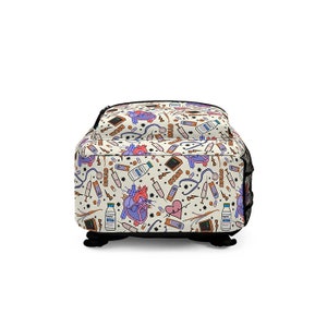 K&ouml;nnte beinhalten: Ein wei&szlig;er Canvas-Rucksack mit einem bunten Muster aus medizinischen Symbolen, darunter ein Herz, Pillen, Spritzen und ein Stethoskop. Das Muster wiederholt sich &uuml;ber den gesamten Rucksack.