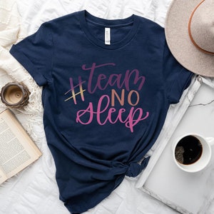 May include: Navy blue t-shirt with the text "#team NO Sleep" in a gradient of pink and yellow. The shirt is styled with a hat, a tray with a coffee cup, a book, and a clock.