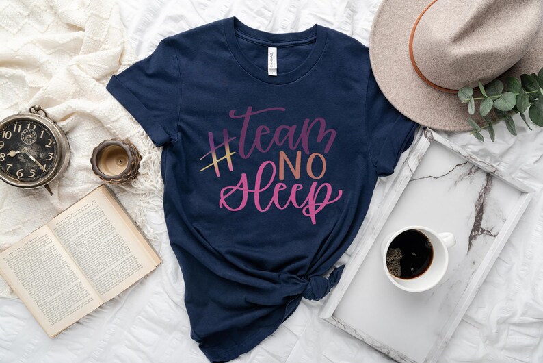 May include: Navy blue t-shirt with the text "#team NO Sleep" in a gradient of pink and yellow. The shirt is styled with a hat, a tray with a coffee cup, a book, and a clock.