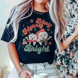 May include: A black t-shirt with a Christmas themed graphic featuring two cartoon teeth wearing Santa hats and the text "Stay Merry & Bright".