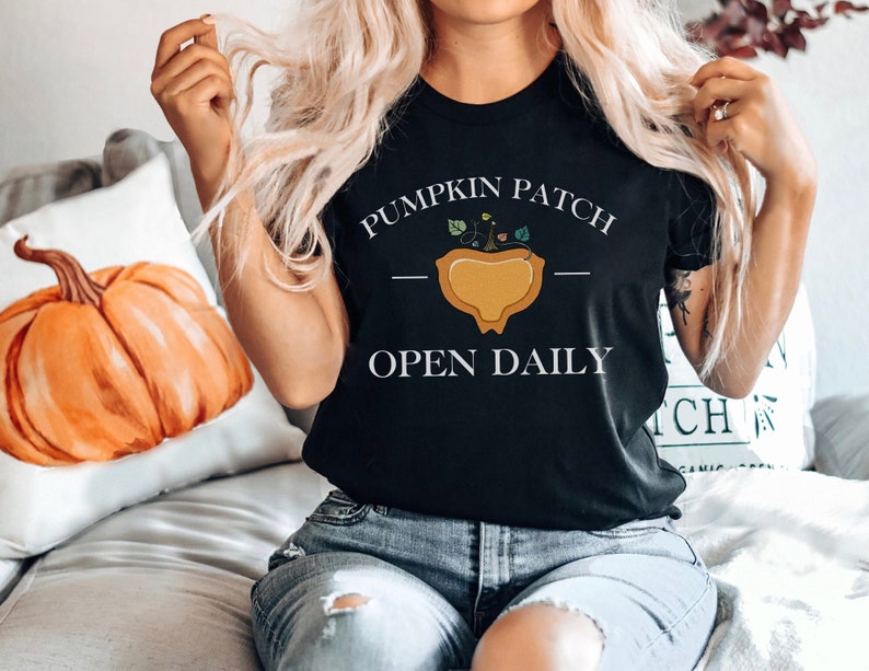 K&ouml;nnte beinhalten: Ein schwarzes T-Shirt mit dem Text "Pumpkin Patch - Open Daily" und einer Grafik einer K&uuml;rbis mit gr&uuml;nen Ranken.