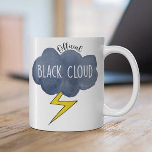 May include: White ceramic mug with a black cloud design, the words "BLACK CLOUD" and "Official" are printed on the mug. A yellow lightning bolt is below the cloud. The mug has a white handle.