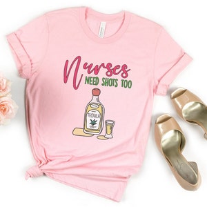 May include: Pink t-shirt with the text "Nurses need shots too" and a cartoon image of a bottle of tequila and a shot glass.