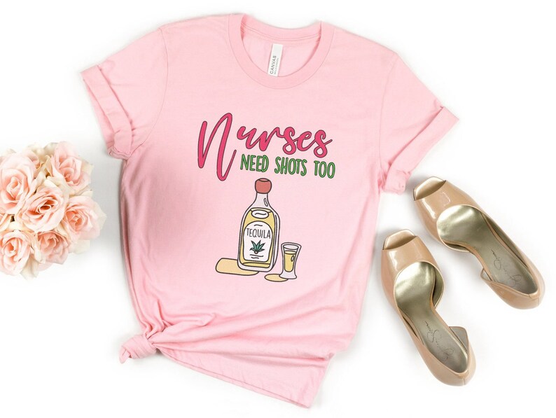May include: Pink t-shirt with the text "Nurses need shots too" and a cartoon image of a bottle of tequila and a shot glass.