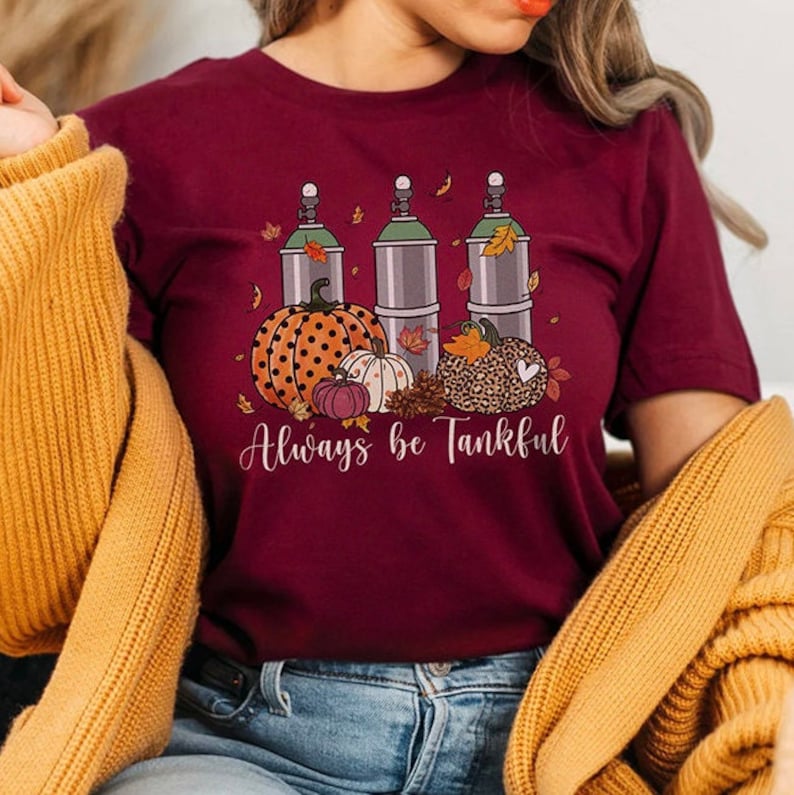 May include: A maroon t-shirt with a graphic of three scuba tanks, pumpkins, and fall leaves. The text "Always be Tankful" is printed below the graphic.