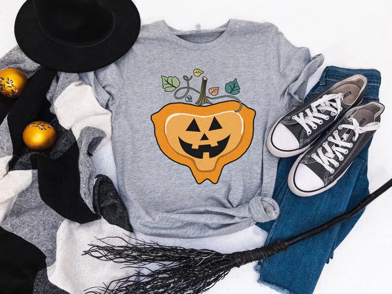 May include: A gray t-shirt with a cartoon orange pumpkin with a jack-o'-lantern face. The pumpkin is on a vine with green leaves.