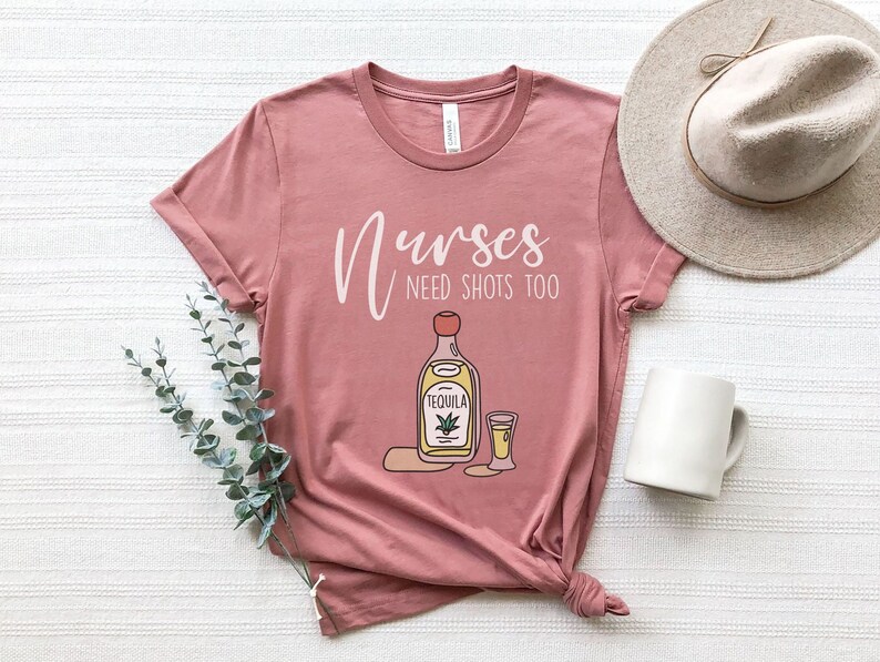 May include: A pink t-shirt with the text "Nurses need shots too" and a cartoon illustration of a bottle of tequila and a shot glass.