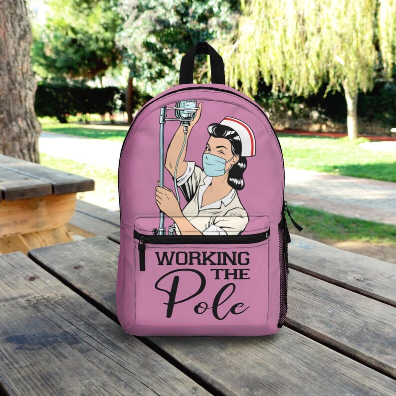 K&ouml;nnte beinhalten: Rosa Rucksack mit einer Cartoon-Abbildung einer Krankenschwester mit Gesichtsmaske, die einen Infusionsst&auml;nder h&auml;lt. Der Text "Working the Pole" ist auf der Vorderseite des Rucksacks aufgedruckt.