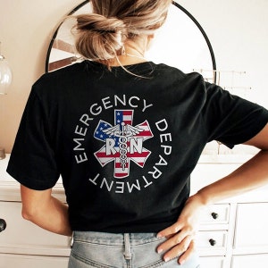 May include: Black t-shirt with a white circle graphic that says "Emergency Department" and features a red, white and blue American flag star of life with a snake and staff medical symbol and the letters "RN" in the centre.