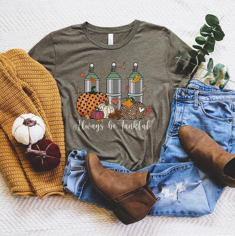 May include: A green t-shirt with a graphic of three silver canisters, pumpkins, and fall leaves. The text "Always be Tankful" is printed below the graphic.
