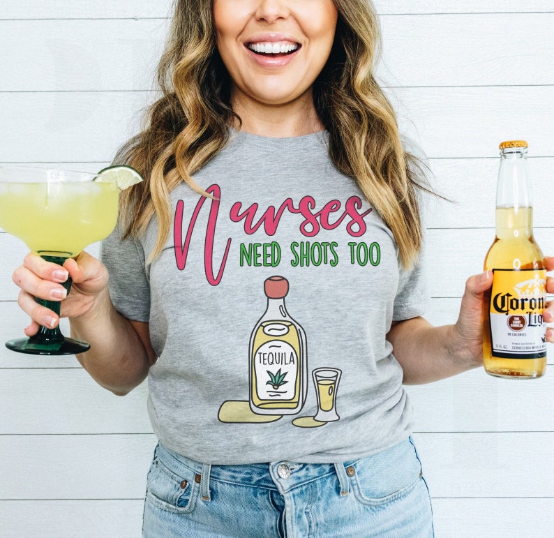 May include: A gray t-shirt with the text "Nurses Need Shots Too" in pink and green. The shirt features a cartoon illustration of a bottle of tequila and a shot glass.