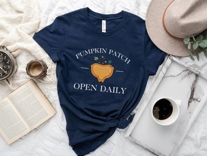 K&ouml;nnte beinhalten: Ein marineblaues T-Shirt mit einer wei&szlig;en Grafik einer K&uuml;rbisplantage mit dem Text "Pumpkin Patch Open Daily".