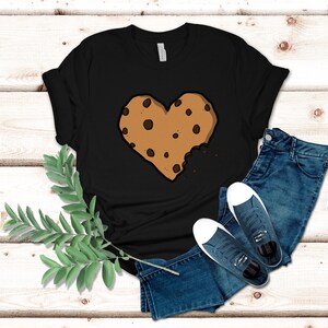 May include: Black t-shirt with a brown chocolate chip cookie in the shape of a heart with a bite taken out of it.