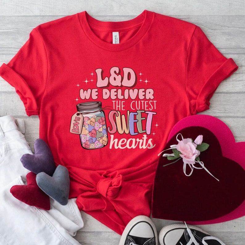 May include: Red t-shirt with a graphic of a jar filled with hearts and the text "L&D We Deliver The Cutest Sweet Hearts".