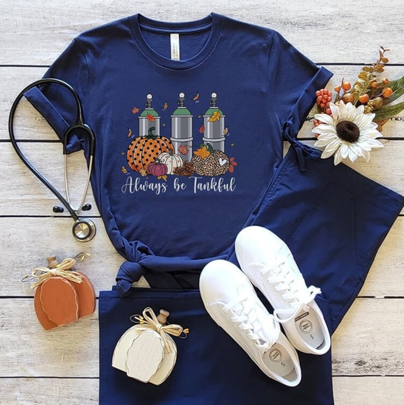 May include: A navy blue t-shirt with a graphic of three oxygen tanks, pumpkins, and fall leaves. The text "Always be Tankful" is printed below the graphic.