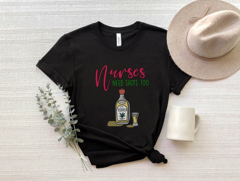 May include: Black t-shirt with the text "Nurses need shots too" in pink and green. A cartoon image of a bottle of tequila and a shot glass are below the text.