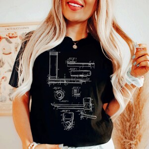 Peut inclure: T-shirt noir avec un graphique blanc d'un dessin de brevet vintage pour un chariot &eacute;l&eacute;vateur. Le dessin comprend des num&eacute;ros et des &eacute;tiquettes.