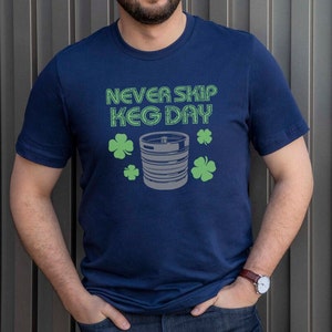 May include: A navy blue t-shirt with the text "NEVER SKIP KEG DAY" in white outlined in green. A gray and white illustration of a keg with green shamrocks is below the text.