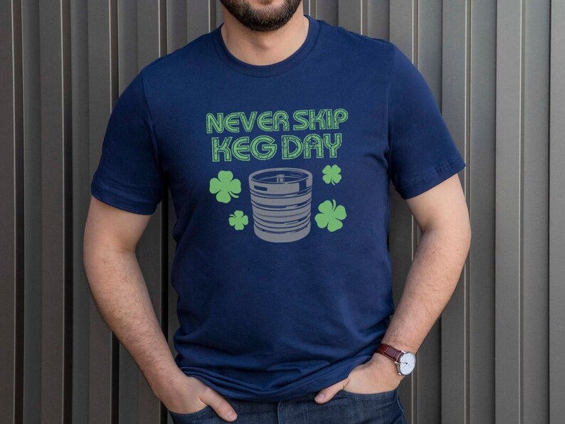 May include: A navy blue t-shirt with the text "NEVER SKIP KEG DAY" in white outlined in green. A gray and white illustration of a keg with green shamrocks is below the text.