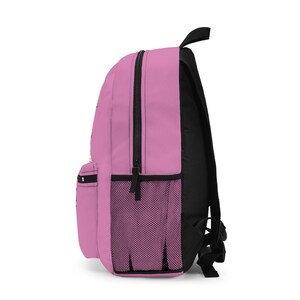 K&ouml;nnte beinhalten: Ein rosa Rucksack mit schwarzen Tr&auml;gern und einer Netztasche an der Seite. Der Rucksack hat einen Rei&szlig;verschluss.