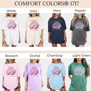 May include: A colour chart of Comfort Colors 1717 t-shirts in shades like white, ivory, navy, and pepper. Each shirt displays a brain graphic with the text "I lobe you" and "but don't worry, it's targeted."