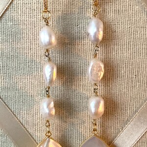 May include: A pair of gold earrings with a teardrop-shaped pearl at the bottom and a chain of smaller pearls going up the earring.