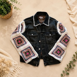 May include: A black denim jacket featuring long sleeves made of white, pink, and dark-toned crochet granny squares. The jacket has a classic collar with white crochet trim, a button-front closure, and two chest pockets with buttoned flaps.