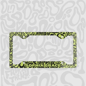 Green and black f1 themed lando norris car license plate frame is shown against a black and white lando norris pattern. With personalised name engraved on the print. 

Lando Norris F1 License Plate Frame: Green and black pattern, Aluminum
